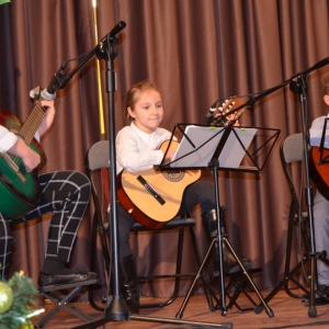 Zdjęcie przedstawia uczniów nauki gry na gitarze podczas występu w Koncercie Noworocznym