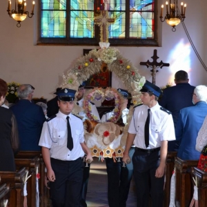 Zdjęcie przedstawia Strażaków wynoszących koronę dożynkową z parkowego kościoła