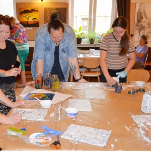 Zdjęcie przedstawia uczestników warsztatów wakacyjnych z mozaiki witrażowej podczas tworzenia mozaiki szklanej